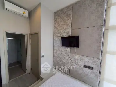 Modern bedroom with wall-mounted TV and air conditioning, featuring a sleek bathroom entrance.