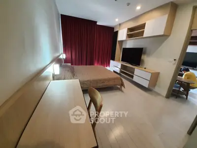 Modern bedroom with sleek furniture and large TV, featuring a cozy workspace and elegant red curtains.