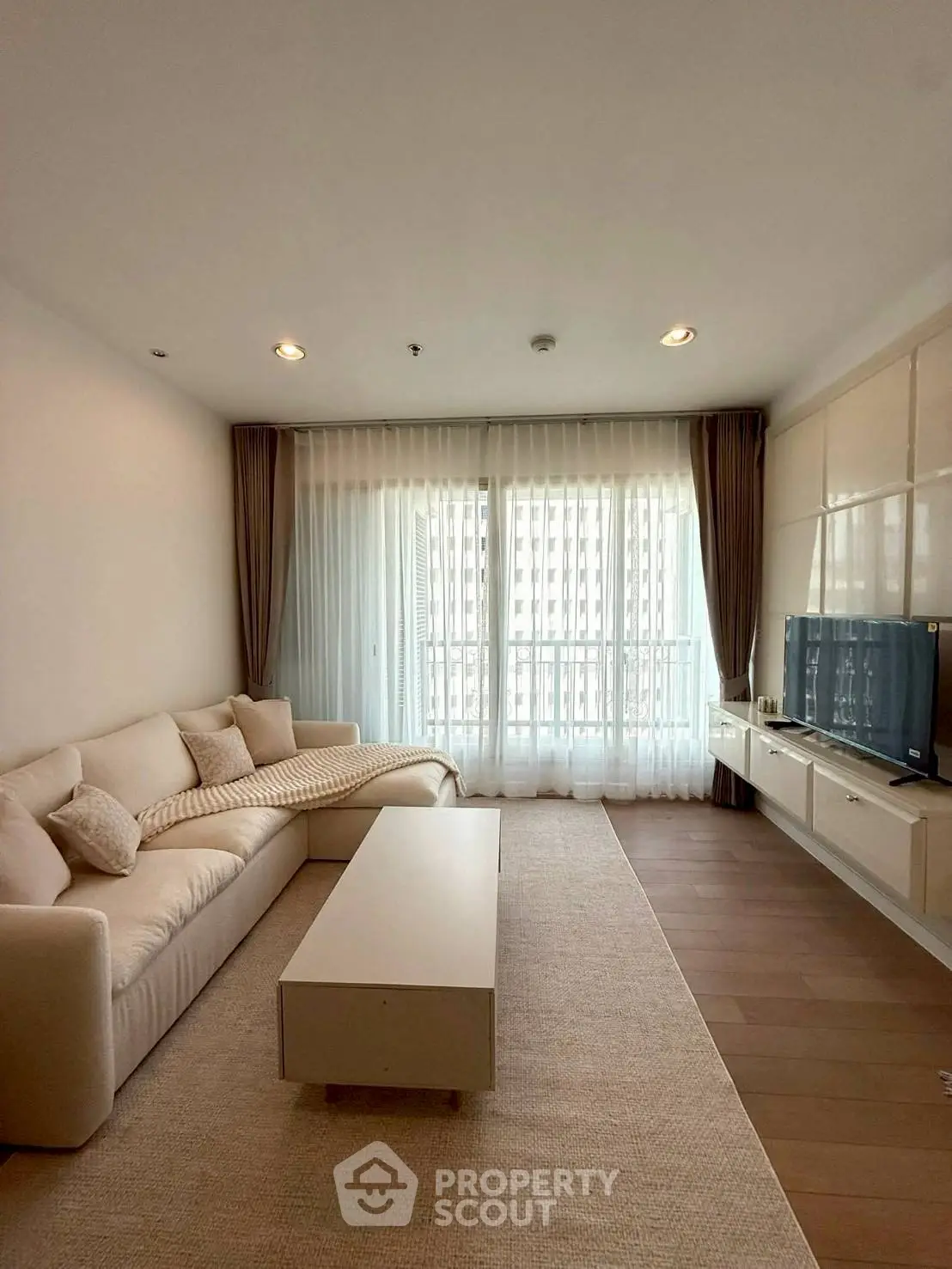 Elegant living room with cozy sofa and modern TV setup, featuring large window for natural light.