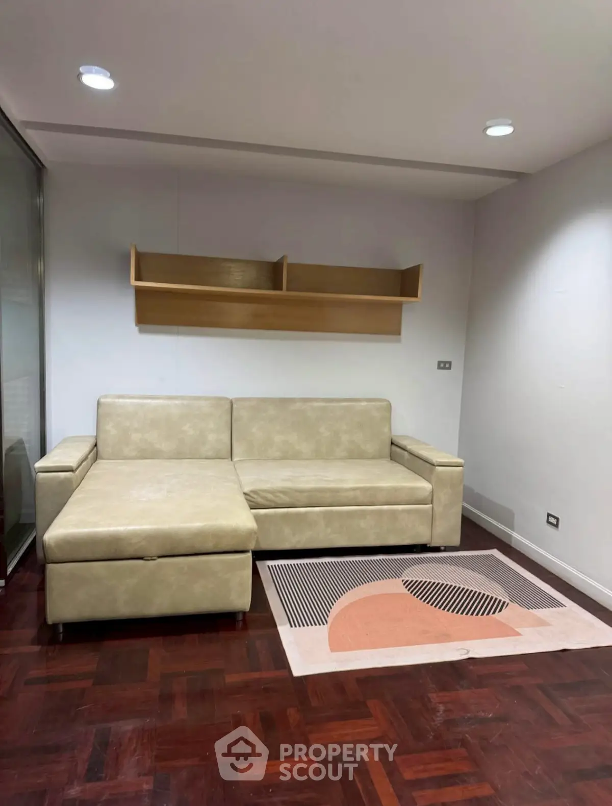 Modern living room with beige sofa and wooden flooring, featuring a stylish wall shelf and contemporary rug.