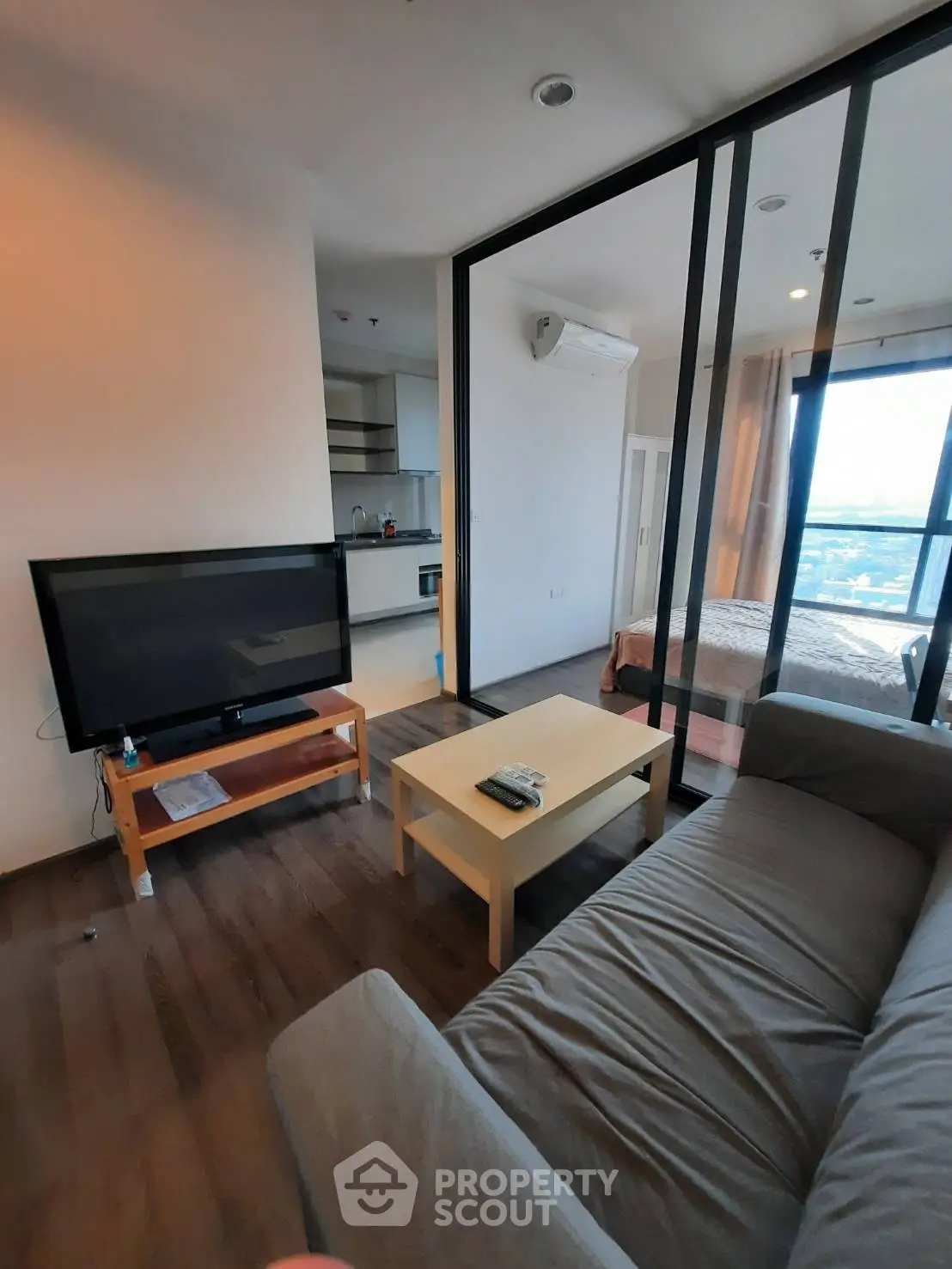 Modern apartment with open living room and kitchen, featuring large windows and a cozy bedroom.
