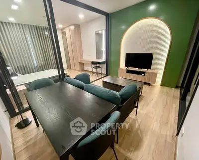 Modern living room with stylish furniture and TV, featuring a green accent wall and wooden flooring.