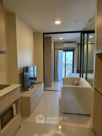 Modern open-plan living room with TV and cozy seating, leading to a bedroom with city view.