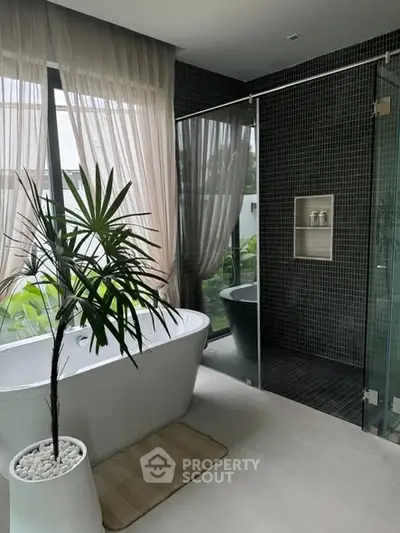 Luxurious bathroom with modern bathtub and glass shower, featuring elegant tile design and lush greenery view.