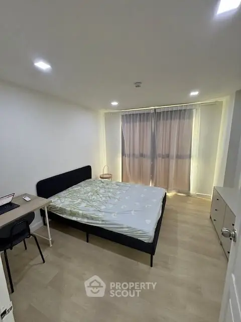 Modern bedroom with natural light, featuring a comfortable bed and workspace, ideal for urban living.