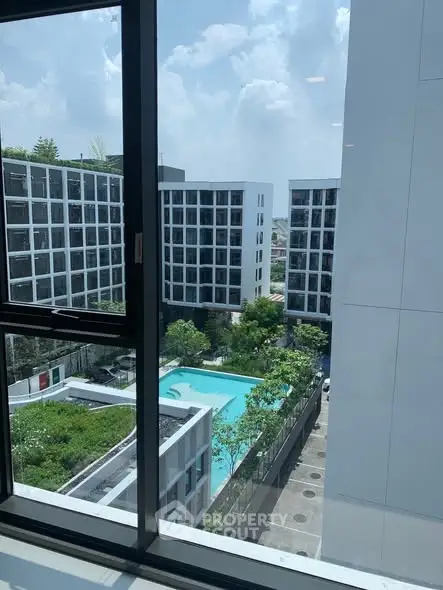 Modern apartment complex with pool view from window, showcasing urban living and lush greenery.