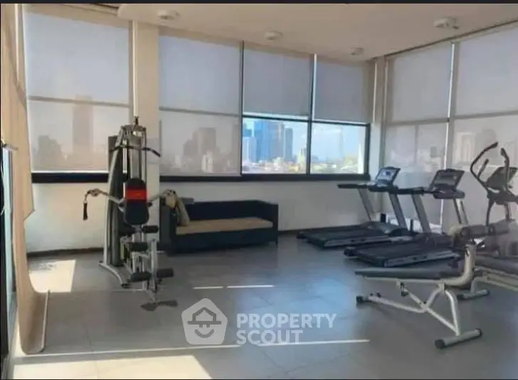 Spacious gym with modern equipment and city view, perfect for fitness enthusiasts.