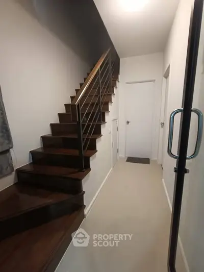 Modern interior hallway with sleek wooden staircase and glass door entrance.