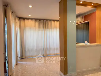 Spacious living room with large windows and elegant curtains, featuring modern lighting and tiled flooring.