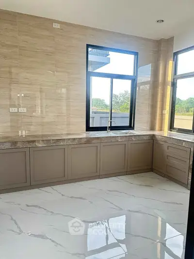 Modern kitchen with marble countertops and large windows offering natural light.