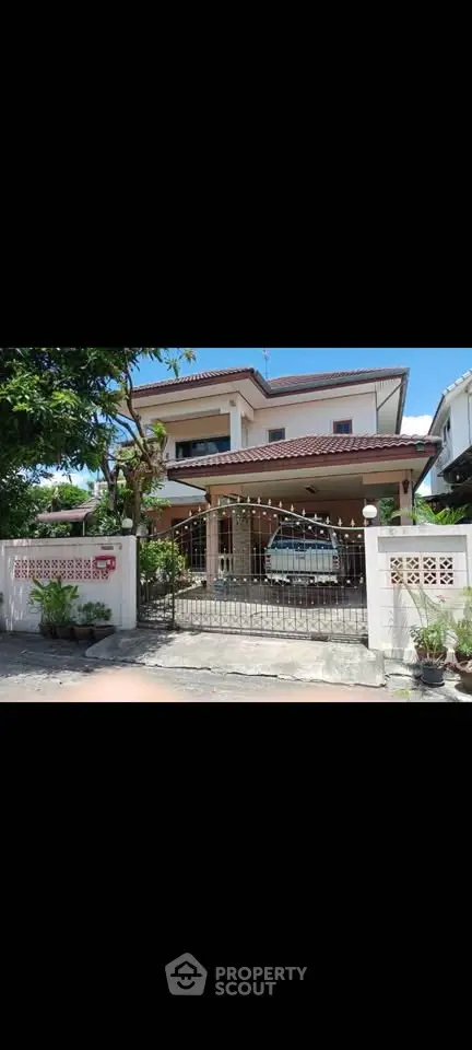 Charming two-story house with gated entrance and lush greenery