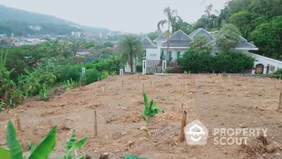 Scenic land plot with lush greenery and distant view of residential area.