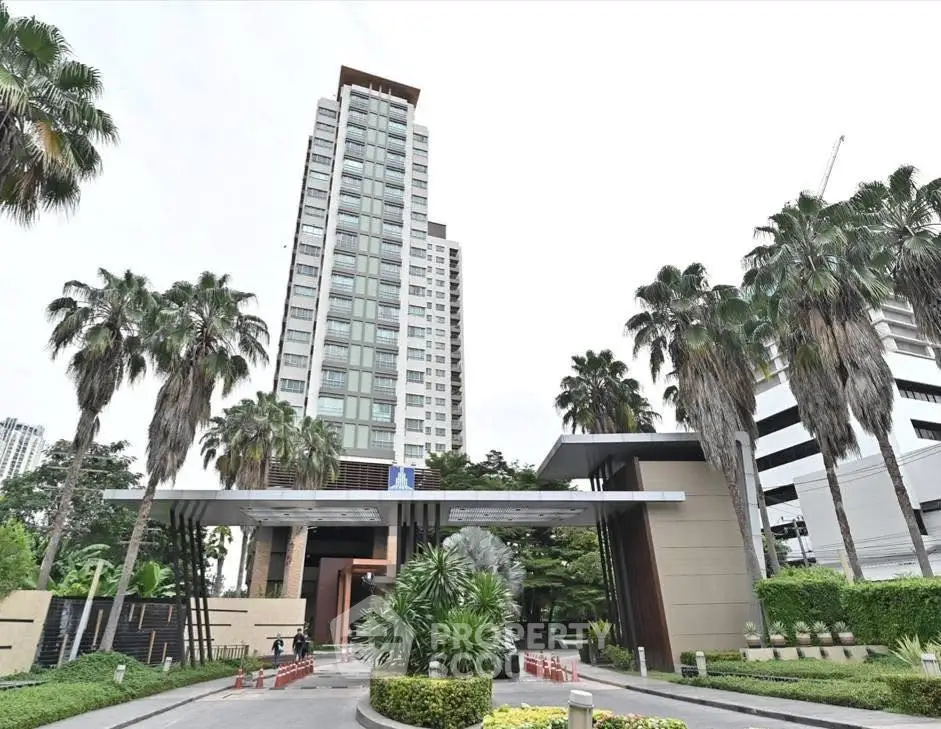 Modern high-rise building with lush landscaping and palm trees at entrance