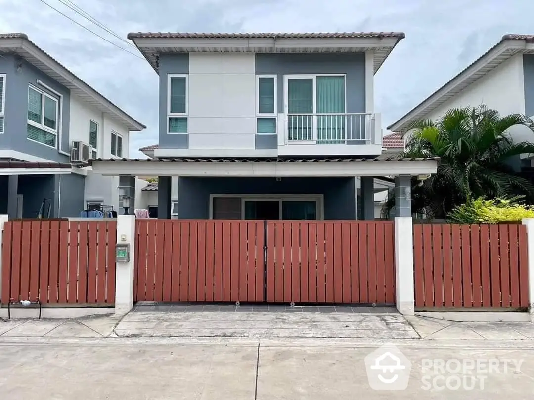 Charming two-story family home with a spacious driveway and secure red fencing, featuring a cozy balcony and modern design.