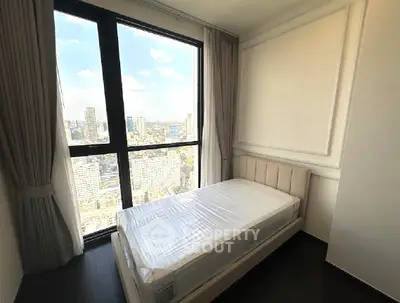 Modern bedroom with stunning city view and large window, featuring a single bed and elegant curtains.