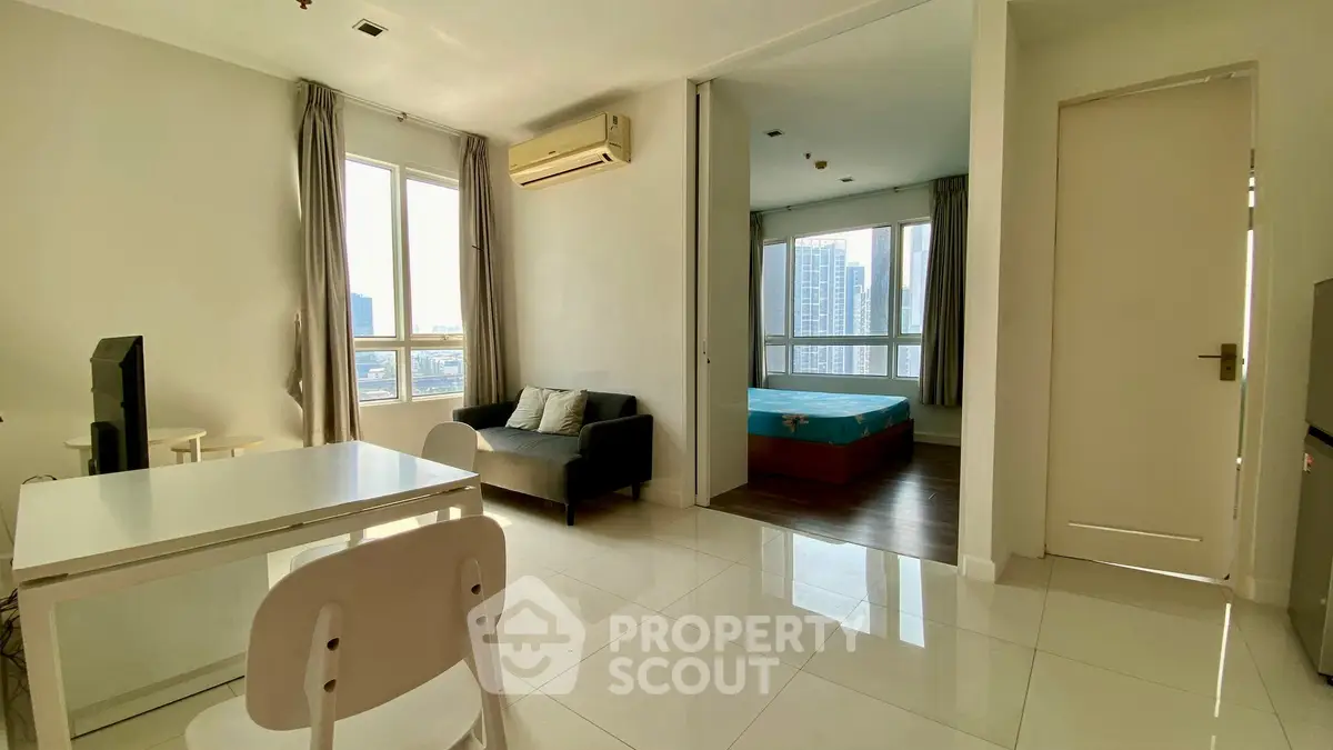 Modern apartment with open living area and bedroom, featuring city views and sleek furnishings.