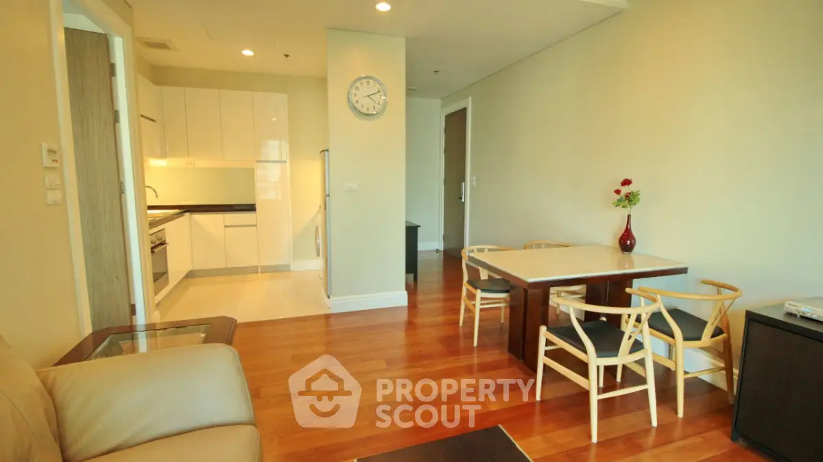 Modern apartment interior with open kitchen and dining area, featuring wooden flooring and stylish furniture.