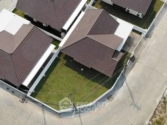 Aerial view of modern residential houses with brown roofs and green lawns in a suburban neighborhood.