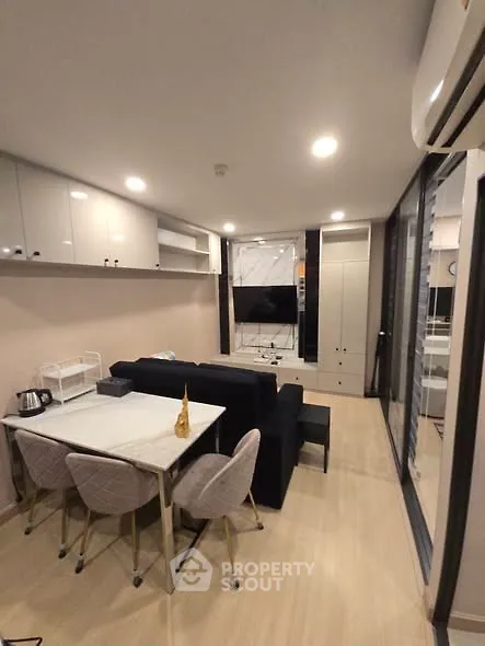 Modern living room with sleek furniture and open layout, featuring a cozy dining area and large TV.
