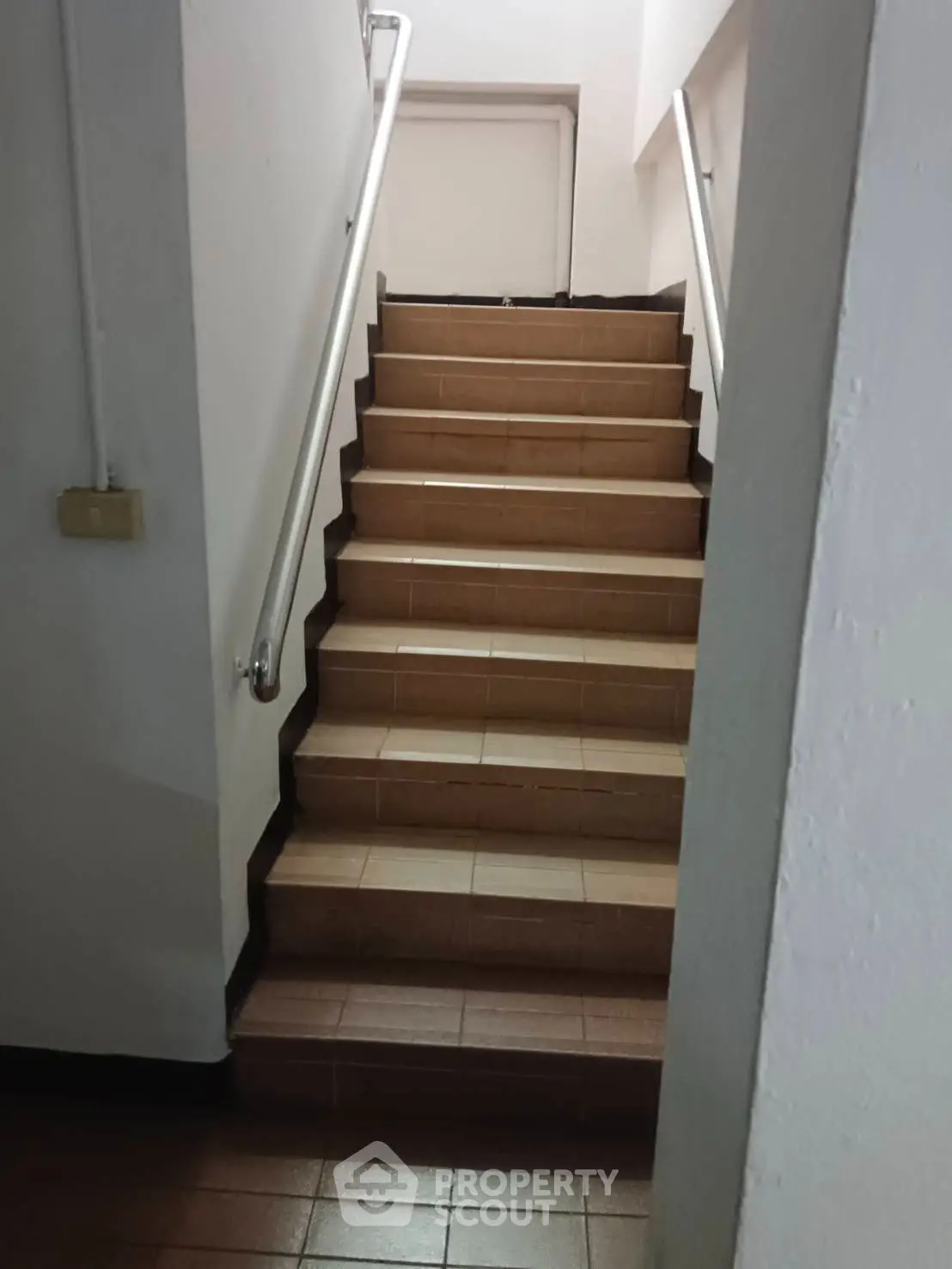 Staircase with brown tiles and metal handrails in a residential building.