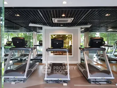 Modern gym with treadmills and mirrored walls in luxury apartment complex.