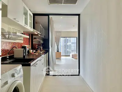 Modern kitchen with open layout and washing machine, leading to a bright living area with large windows.