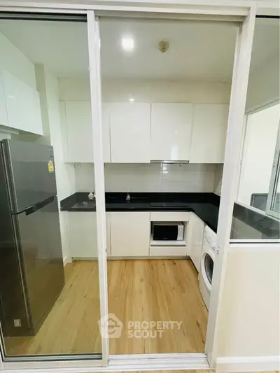 Modern kitchen with sleek white cabinets, black countertops, and wooden flooring, featuring a fridge and washing machine.