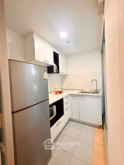 Modern compact kitchen with sleek white cabinets and stainless steel appliances.