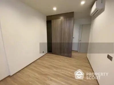 Spacious and modern living area with elegant wooden flooring, crisp white walls, and a sleek air conditioning unit, perfect for contemporary living.