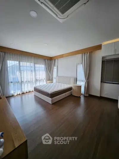 Spacious bedroom with large windows and wooden flooring, offering ample natural light and modern design.