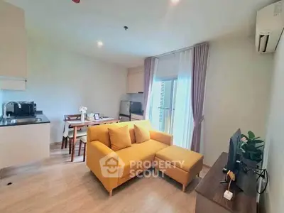 Modern living room with yellow sofa, open kitchen, and natural light from large window.