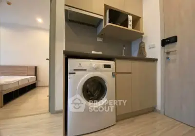 Modern apartment with compact kitchen featuring washing machine and microwave, adjacent to a cozy bedroom.