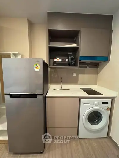 Modern compact kitchen with fridge, washing machine, and sleek cabinetry in a stylish apartment.