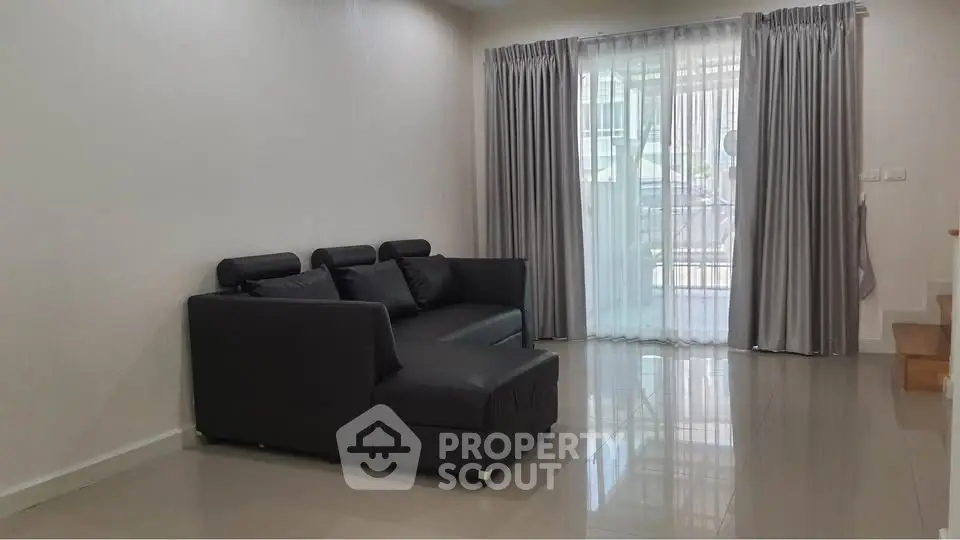 Modern living room with sleek black sofa and large window with curtains