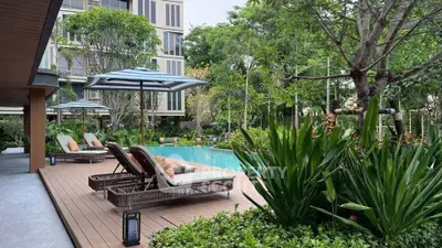 Luxurious poolside area with sun loungers and lush greenery in modern residential complex.