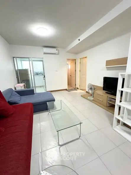 Modern living room with red and blue sofas, glass coffee table, and TV unit in a bright apartment.