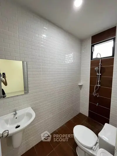 Modern bathroom with white tiles and brown floor, featuring a shower and toilet.