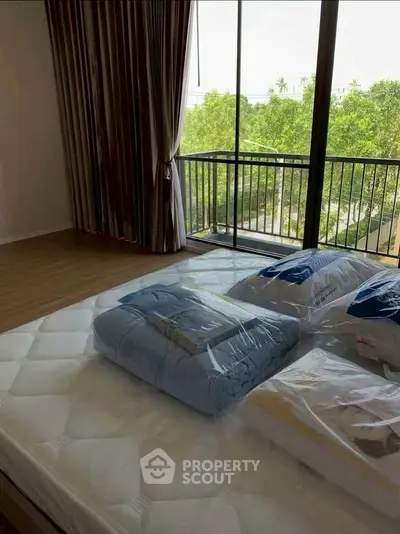 Spacious bedroom with large windows and balcony overlooking lush greenery.