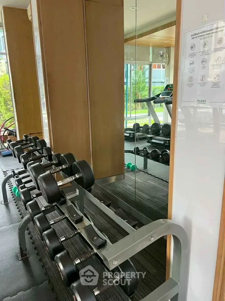 Modern gym with dumbbells and treadmill in luxury apartment complex.