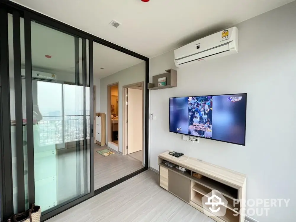 Modern living room with sliding glass doors and wall-mounted TV in a high-rise apartment.