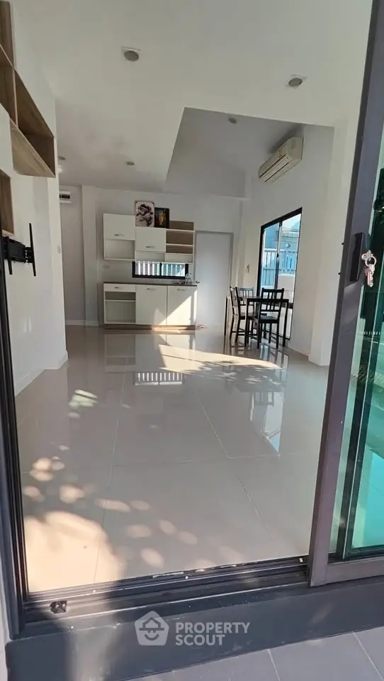 Spacious modern living room with open kitchen and dining area, featuring large windows and sleek tile flooring.