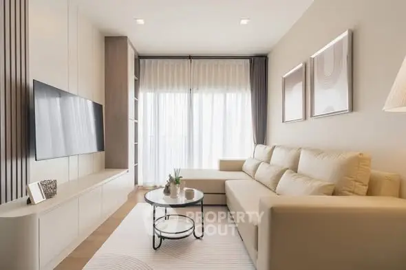 Modern living room with beige sofa, wall-mounted TV, and large window for natural light.