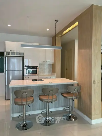 Modern kitchen with sleek island, bar stools, and built-in appliances in a stylish open layout.