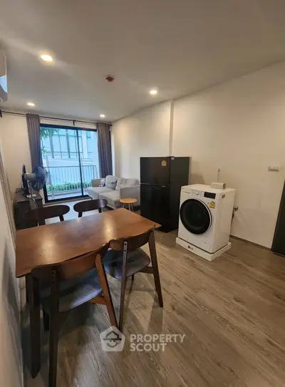 Modern living room with dining area and washing machine, featuring sleek furniture and natural light.