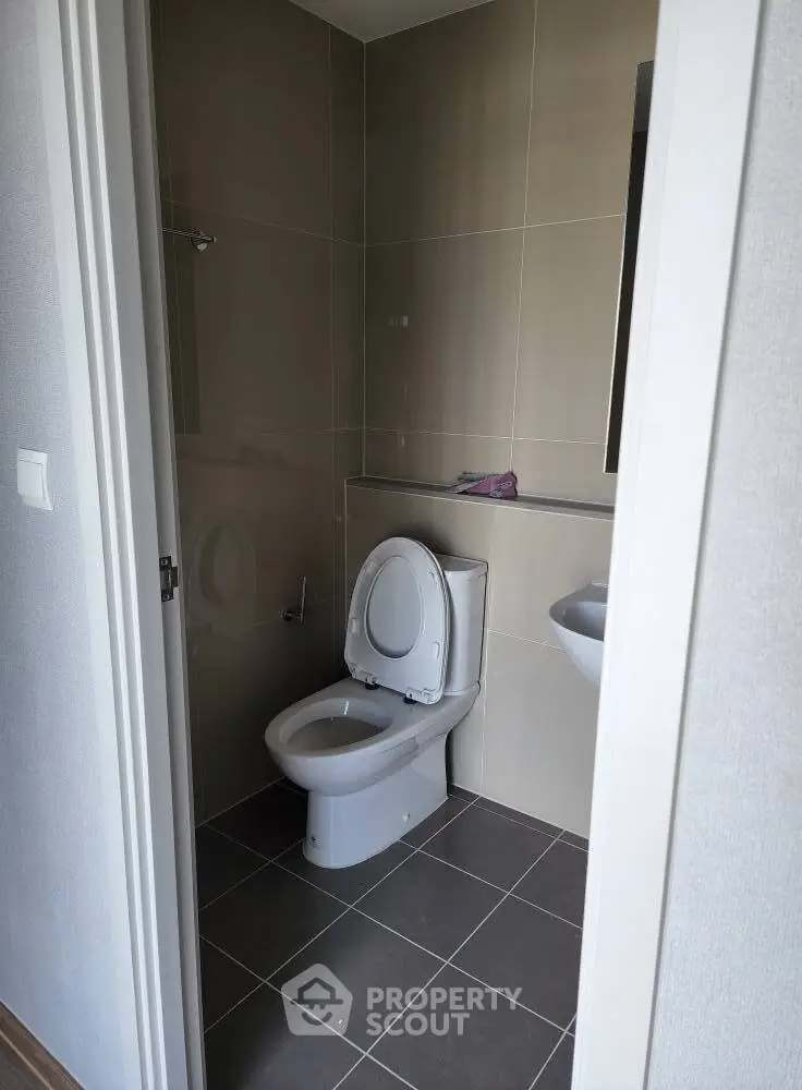 Modern bathroom with sleek design and neutral tones, featuring a toilet and compact sink.