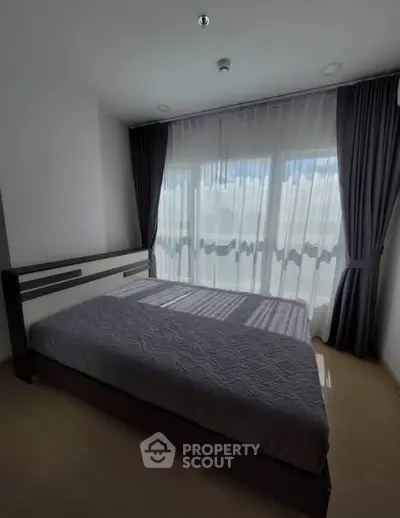 Spacious bedroom with large window and elegant curtains, offering abundant natural light and serene ambiance.