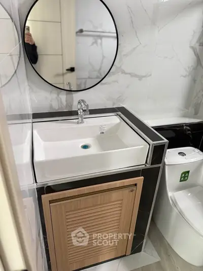 Modern bathroom with sleek sink and round mirror, elegant marble tiles.