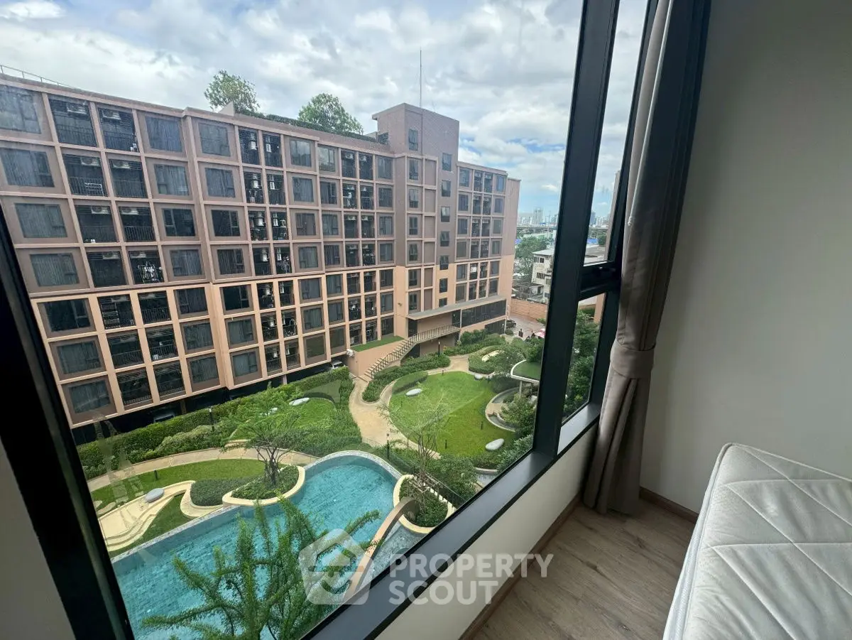 Stunning view from window overlooking modern building and lush garden with pool.