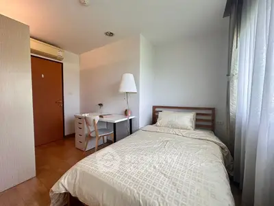 Cozy bedroom with natural light, featuring a single bed, desk, and modern decor, perfect for a peaceful retreat.