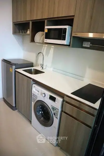 Modern compact kitchen with washing machine, microwave, and sleek cabinetry.
